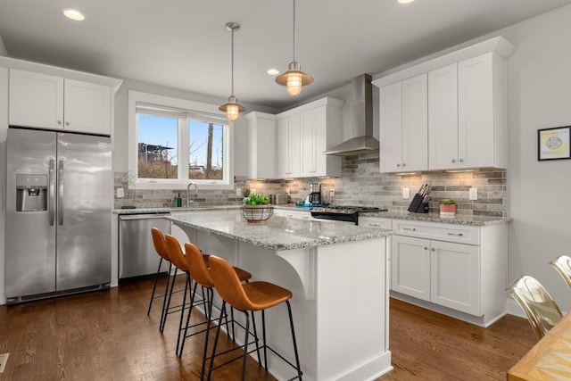 kitchen featuring appliances with stainless steel finishes, a center island, white cabinets, and wall chimney range hood