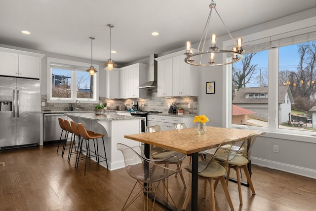 kitchen featuring a center island, pendant lighting, stainless steel appliances, white cabinetry, and wall chimney exhaust hood