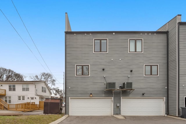 rear view of property with a garage, driveway, and central air condition unit