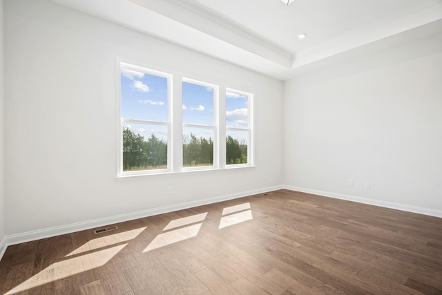 spare room featuring a tray ceiling, recessed lighting, visible vents, wood finished floors, and baseboards