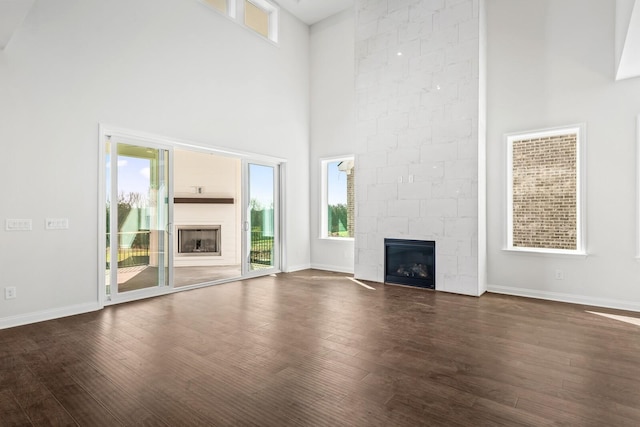 unfurnished living room featuring a large fireplace, a high ceiling, and dark wood-style floors