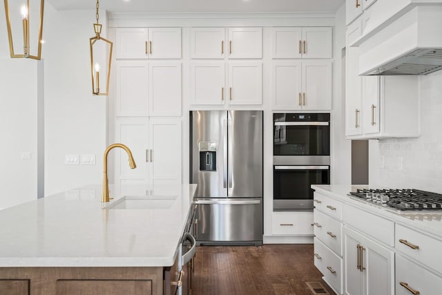 kitchen featuring a center island with sink, custom range hood, appliances with stainless steel finishes, hanging light fixtures, and a sink