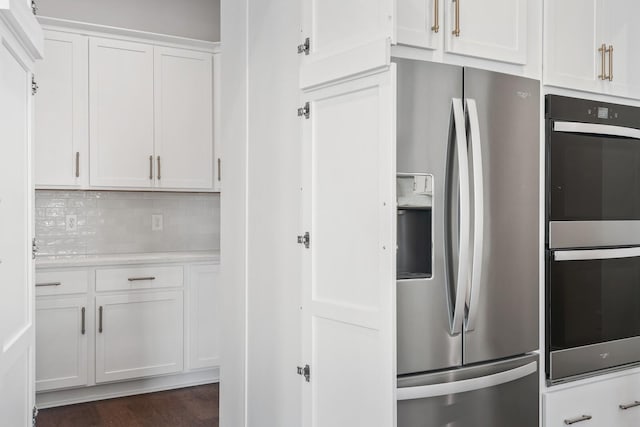 kitchen featuring tasteful backsplash, light countertops, multiple ovens, white cabinets, and stainless steel fridge