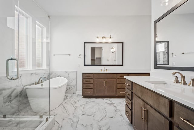 full bath with marble finish floor, two vanities, a freestanding tub, and a sink