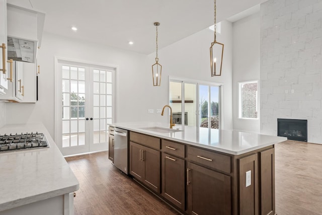 kitchen featuring a center island with sink, decorative light fixtures, stainless steel appliances, french doors, and a sink