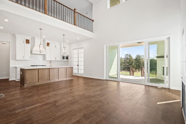 unfurnished living room with recessed lighting, a high ceiling, a sink, baseboards, and dark wood finished floors