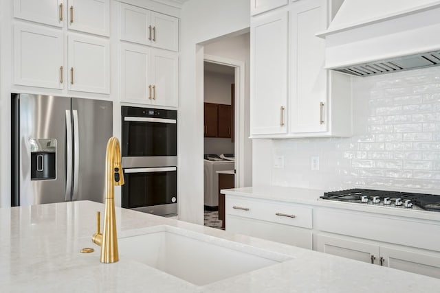 kitchen featuring stainless steel appliances, decorative backsplash, white cabinets, light stone countertops, and premium range hood