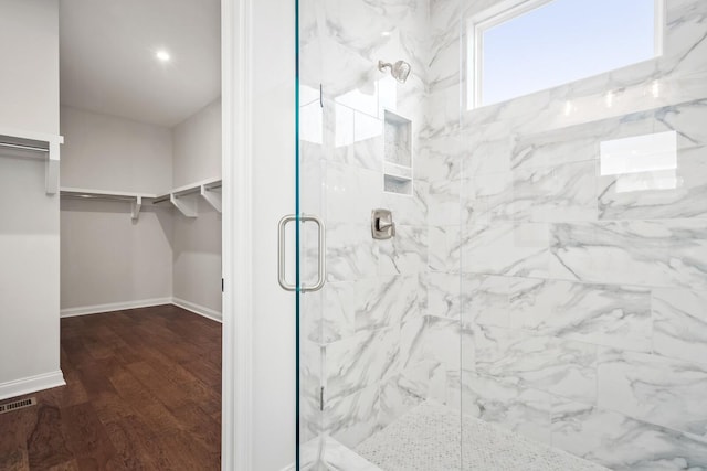 full bath featuring wood finished floors, visible vents, baseboards, a shower stall, and a walk in closet