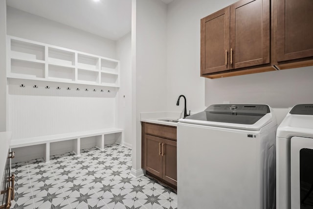 clothes washing area with a sink, baseboards, cabinet space, light floors, and washing machine and clothes dryer