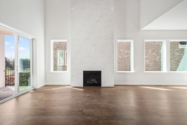 unfurnished living room featuring a premium fireplace, dark wood finished floors, a towering ceiling, and baseboards