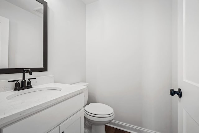 half bath featuring baseboards, vanity, toilet, and wood finished floors