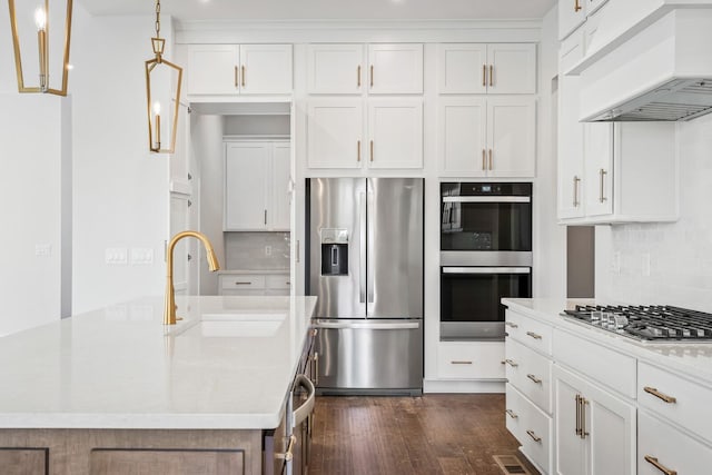 kitchen featuring custom range hood, hanging light fixtures, appliances with stainless steel finishes, a sink, and an island with sink