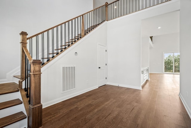 staircase featuring a towering ceiling, baseboards, visible vents, and wood finished floors