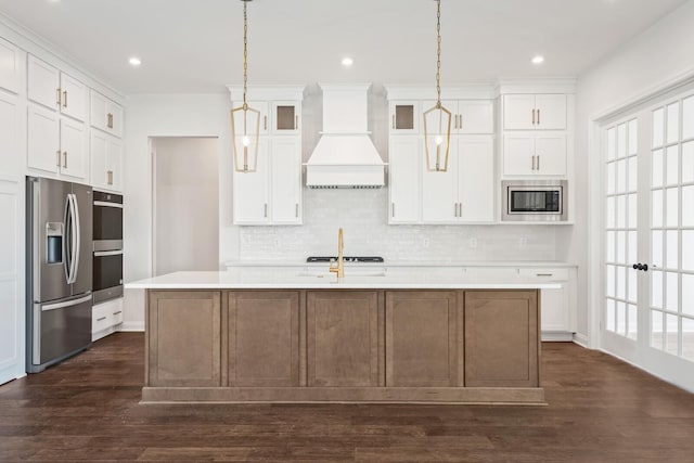 kitchen featuring an island with sink, appliances with stainless steel finishes, custom exhaust hood, light countertops, and white cabinetry