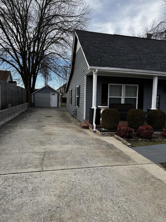 view of side of property featuring a porch, an outbuilding, concrete driveway, and roof with shingles