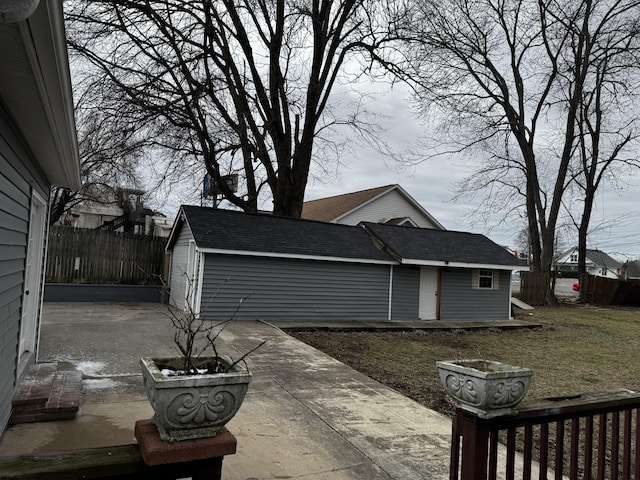 view of side of property with an outbuilding, roof with shingles, a lawn, a patio area, and fence