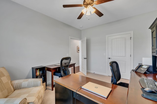office featuring baseboards, a ceiling fan, and light carpet