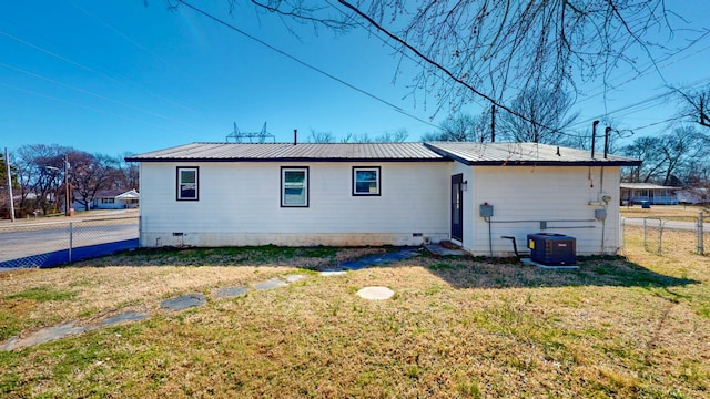 rear view of house with a yard, central AC unit, crawl space, metal roof, and fence