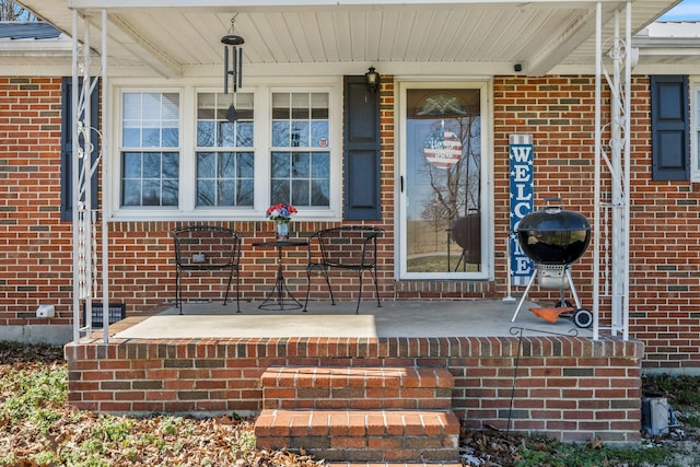 doorway to property featuring a porch and brick siding