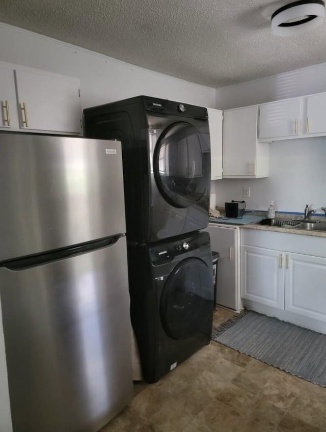 clothes washing area featuring a textured ceiling, laundry area, stacked washer / dryer, and a sink