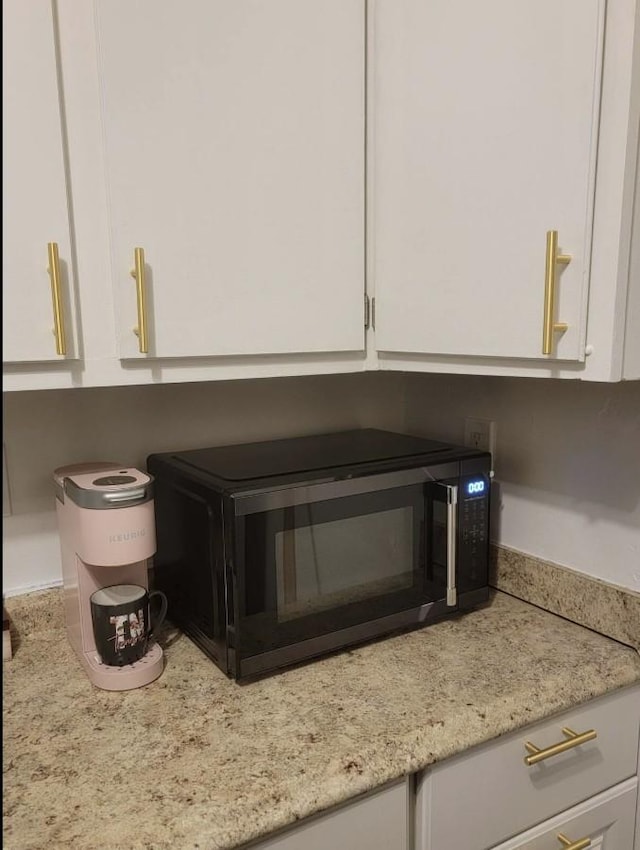 details with black microwave, white cabinetry, and light stone countertops