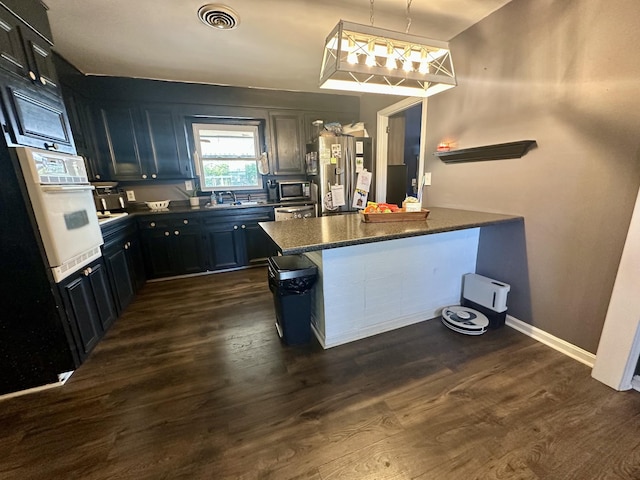 kitchen with visible vents, dark wood-style flooring, a peninsula, stainless steel appliances, and a sink