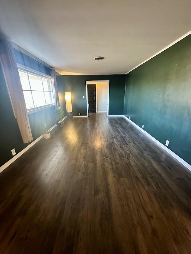 spare room with ornamental molding, dark wood-type flooring, visible vents, and baseboards