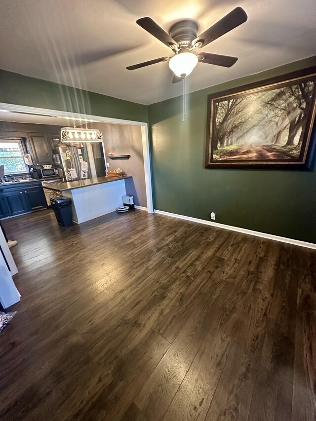 unfurnished living room with a ceiling fan, baseboards, and dark wood-style flooring