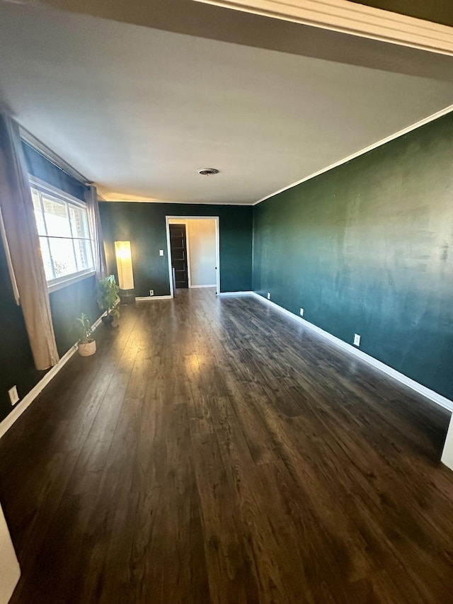 spare room featuring dark wood-style floors, ornamental molding, visible vents, and baseboards