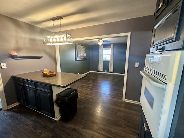 kitchen with dark wood-style floors, white oven, dark cabinetry, and baseboards