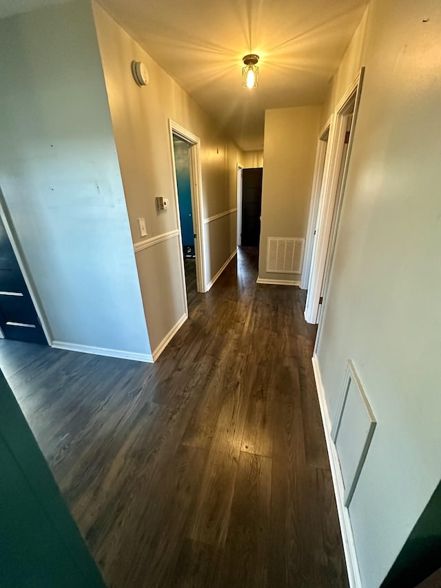 corridor with dark wood-type flooring, visible vents, and baseboards