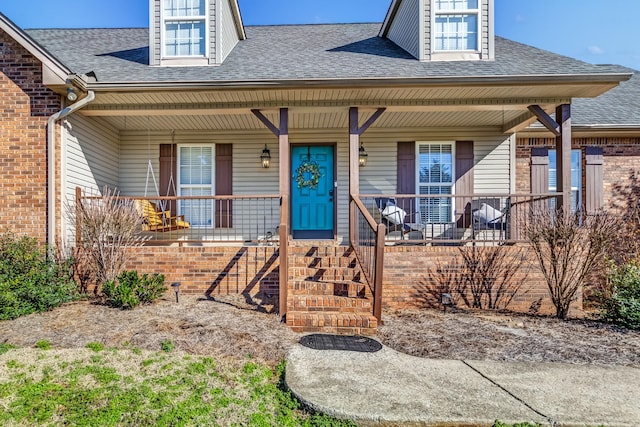 view of front of property featuring covered porch, roof with shingles, and brick siding