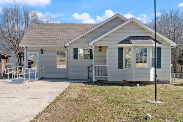 view of front of home with a shingled roof, a front yard, and fence