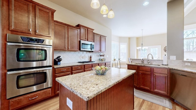 kitchen featuring light wood-style flooring, a sink, appliances with stainless steel finishes, light stone countertops, and tasteful backsplash