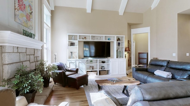 living room featuring a towering ceiling, light wood-style flooring, a fireplace, and beamed ceiling