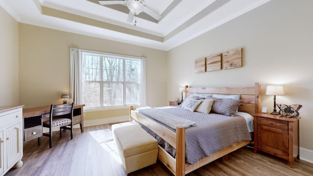 bedroom featuring ornamental molding, a tray ceiling, baseboards, and wood finished floors