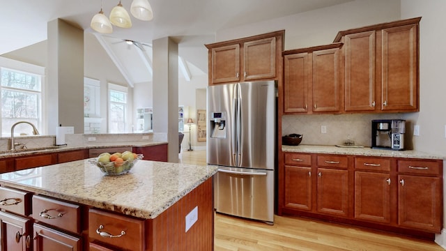 kitchen featuring tasteful backsplash, light stone counters, light wood-type flooring, stainless steel refrigerator with ice dispenser, and a sink