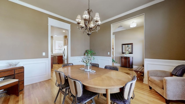 dining area with wainscoting, light wood-type flooring, an inviting chandelier, and crown molding