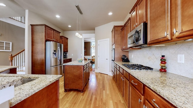 kitchen with light wood finished floors, decorative backsplash, a kitchen island, light stone countertops, and stainless steel appliances