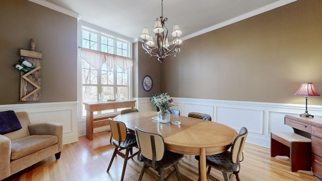 dining room with ornamental molding, wainscoting, light wood-style floors, and a notable chandelier