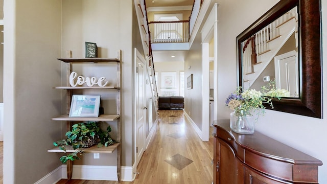 hall with stairs, a high ceiling, light wood-style flooring, and baseboards