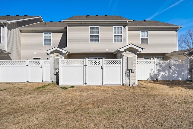 rear view of property featuring a gate, a fenced backyard, and a lawn