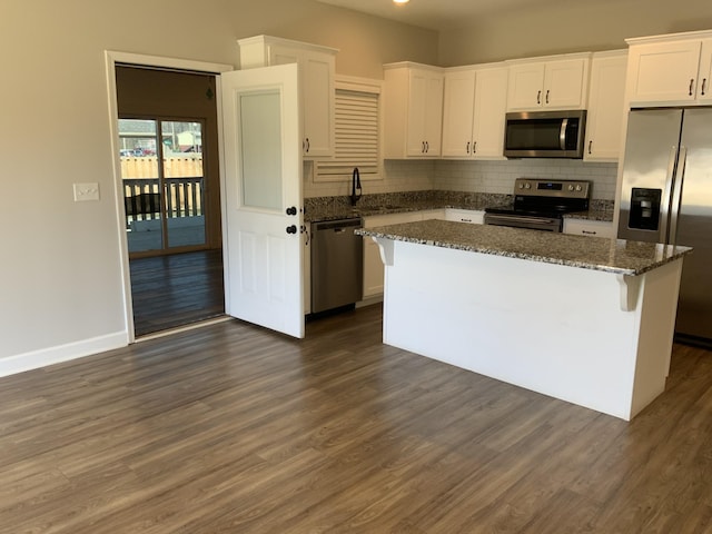 kitchen featuring dark wood-style floors, a kitchen island, dark stone countertops, stainless steel appliances, and white cabinetry