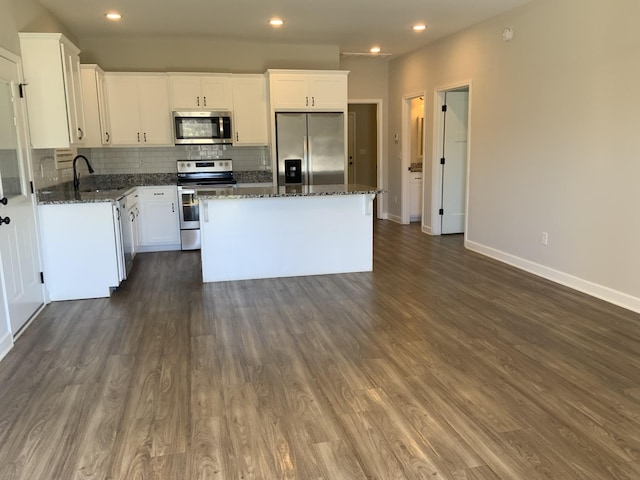 kitchen with appliances with stainless steel finishes, a center island, white cabinets, and dark stone countertops