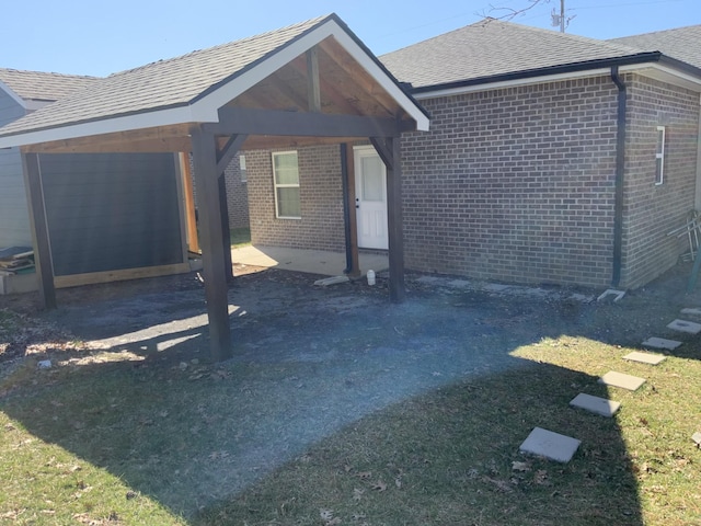 view of front facade featuring a shingled roof, brick siding, and a carport