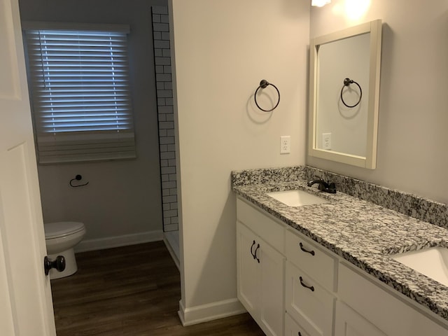 full bath with toilet, wood finished floors, a sink, baseboards, and double vanity