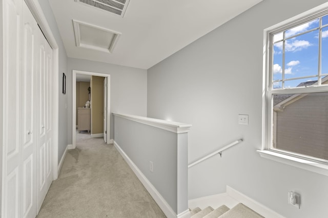 corridor with attic access, visible vents, baseboards, light colored carpet, and an upstairs landing