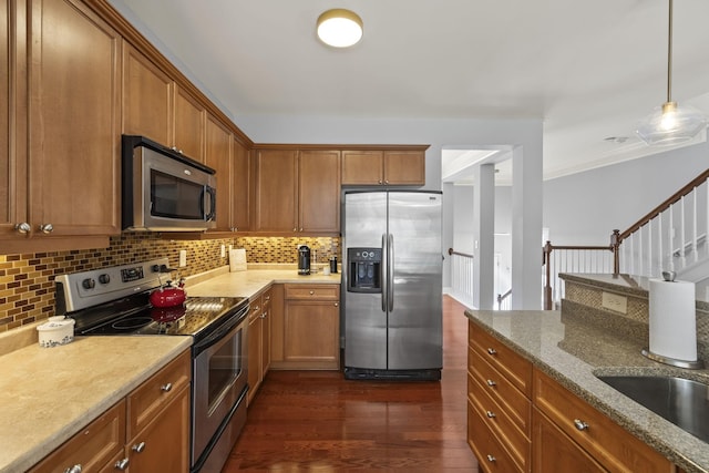 kitchen with appliances with stainless steel finishes, brown cabinets, dark wood-style flooring, and pendant lighting