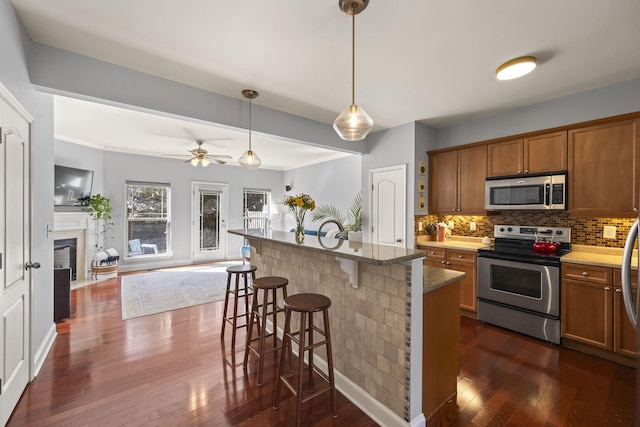 kitchen with a breakfast bar, brown cabinets, stainless steel appliances, hanging light fixtures, and open floor plan