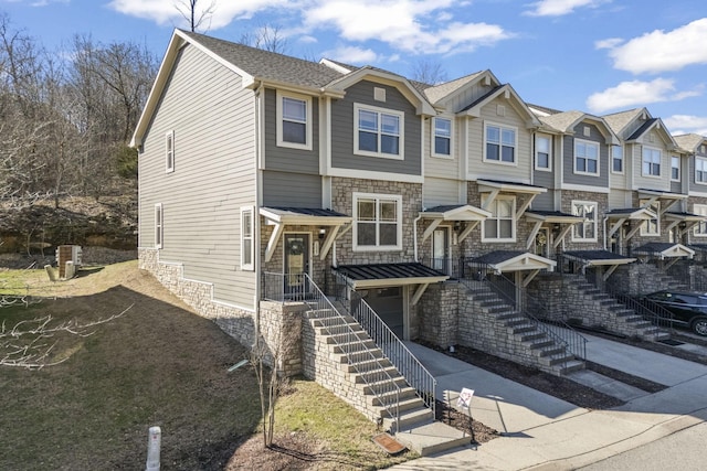 view of front facade featuring driveway, stone siding, an attached garage, and a residential view